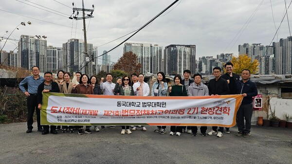[사진: 구룡마을에서 동국대학교 법무대학원 도시정비법무정책최고위2기 기념촬영 모습, 멀리 개포주공아파트 모습이 겹친다.@한국도시환경헤럴드]